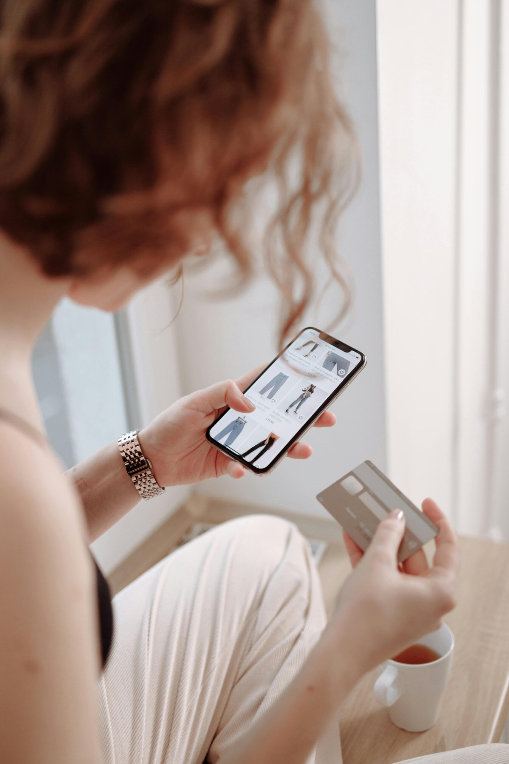 A lady scrolls her phone looking at clothing and has her credit card ready to buy. Used to show customer experience metrics.